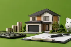 Maquette d'une maison neuve sur fond vert, avec une calculatrice, des piles de pièces, une tirelire et un porte-bloc